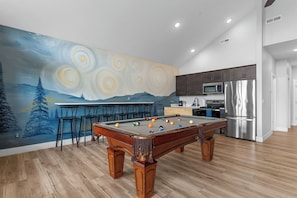 Une table de billard avec des billes, une cuisine équipée et une fresque murale.
