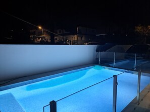 Une piscine dotée d’une paroi en verre et d’un bord carrelé, entourée d’un petit muret et avec un lampadaire en arrière-plan.