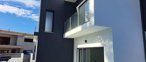 A modern two-story house with a balcony, a swimming pool, and a clear blue sky.