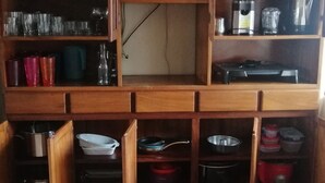 Eine Küche mit Holzausstattung, Regalen und diversen Küchenutensilien, darunter Tassen, Teller, Gläser und Kochgeschirr.