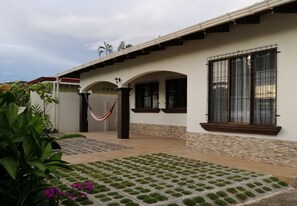 A house with a tiled patio, a hammock, and a window with bars. - Casa Langosta c/ Piscina Privada (Jacó)