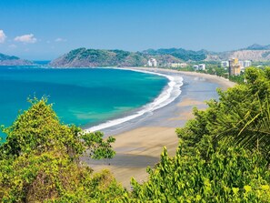 A coastal landscape with a sandy beach, clear blue waters, and dense green vegetation. - Casa Langosta c/ Piscina Privada (Jacó)
