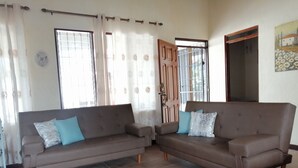 Ein Wohnzimmer mit zwei Sofas, einer Holztür und einem Fenster mit Gitterstäben.