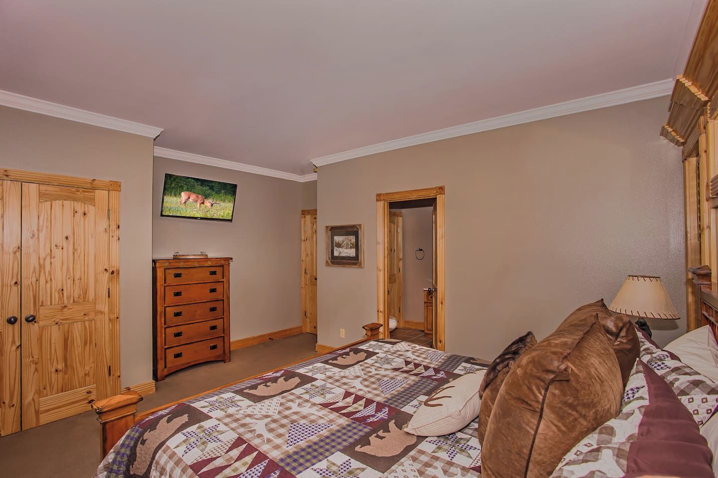 A bedroom with a bed, dresser, and a television on the wall.