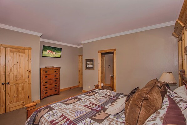 A bedroom with a bed, dresser, and a television on the wall.