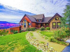 A two-story house with a stone facade, a wrap-around porch, and a landscaped front yard with a stone pathway.