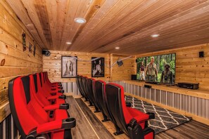 A row of red and black cinema seats with a large screen displaying a movie.