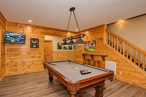 Een pooltafel in een ruimte met houten wanden en een trap.