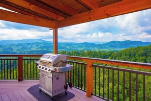 A barbecue grill on a wooden deck with a view of green mountains.