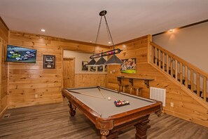 A pool table in a room with wooden walls and a staircase.