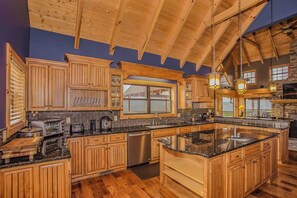 A spacious kitchen with wooden cabinets, a large island, and a stone fireplace.