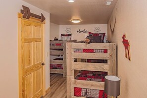 Ein gemütliches Zimmer mit einem Etagenbett, einer Holztür, einer Wand mit einer Bärenillustration und einer Lampe.