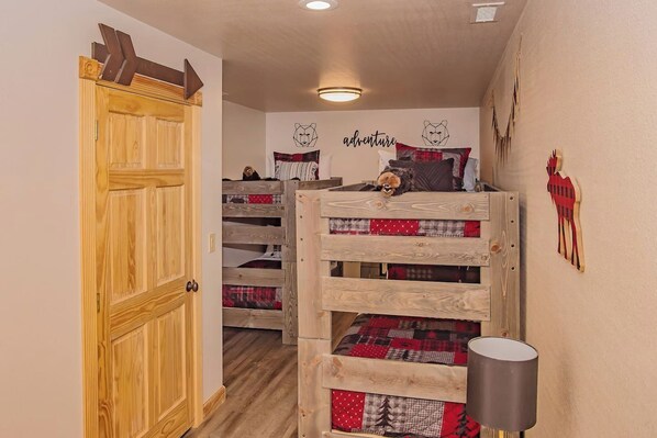 A cozy room with a bunk bed, a wooden door, a wall with a bear illustration, and a lamp.