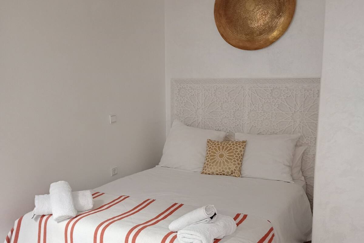 A neatly made bed with striped bedding and rolled towels, a decorative wall plate, and a patterned headboard.