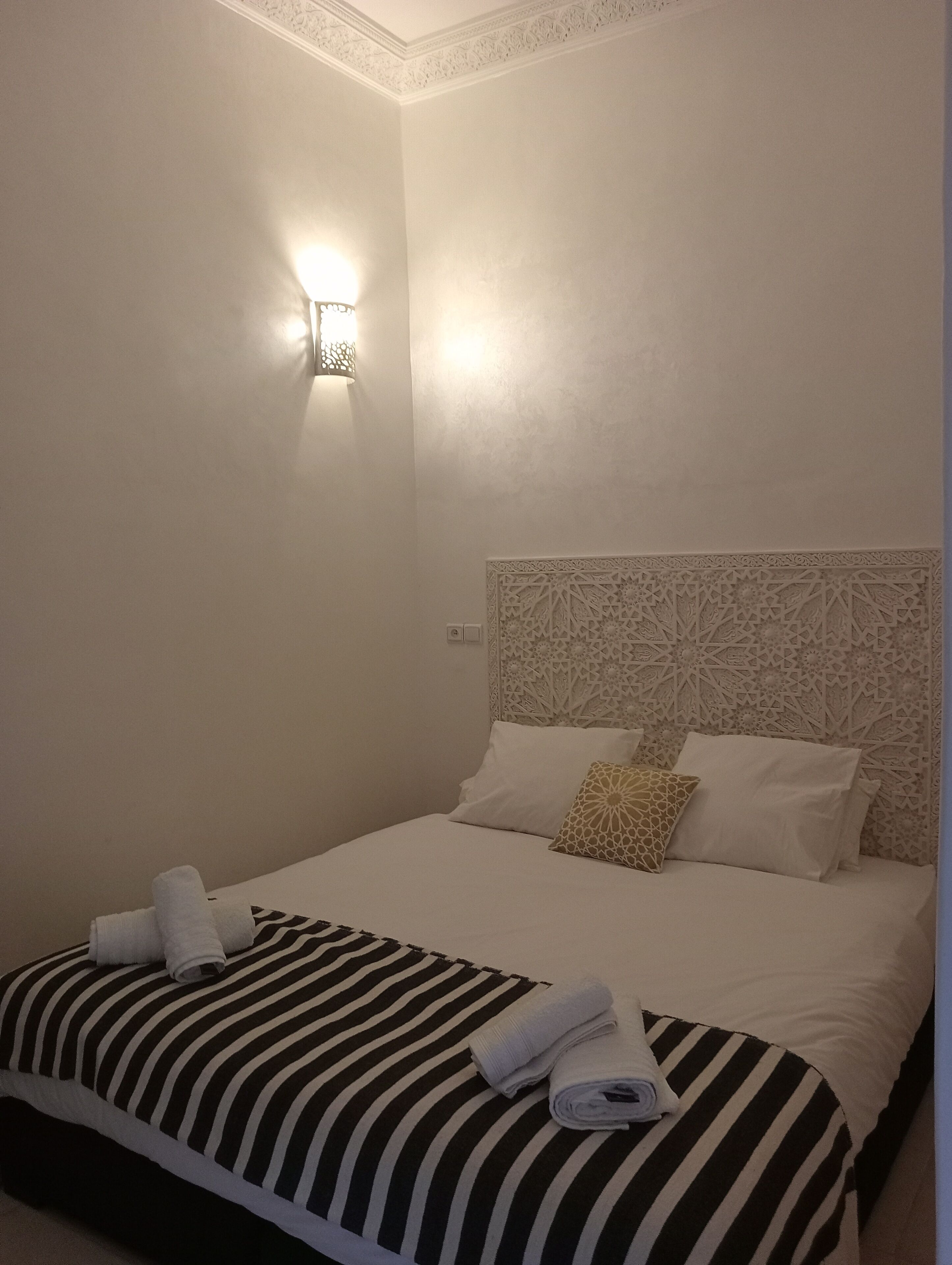 Una habitación de hotel con una cama bien hecha, una lámpara de pared y un cabecero decorativo.