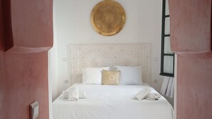 A bedroom with a white bed, a decorative round wall hanging, and a tiled floor with a diamond pattern. - Riad étoile ocre  (Marrakech)