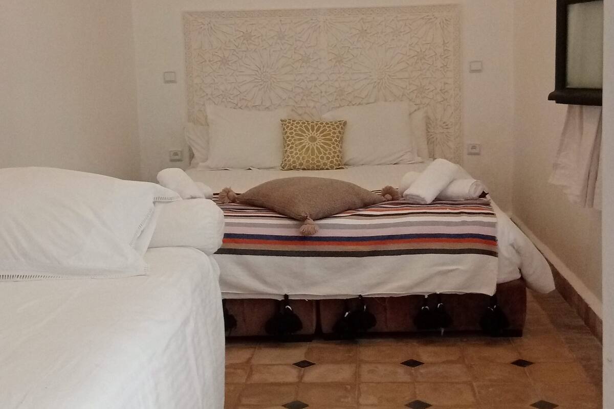 A small, neatly arranged bedroom with a single bed, a nightstand, and a window.