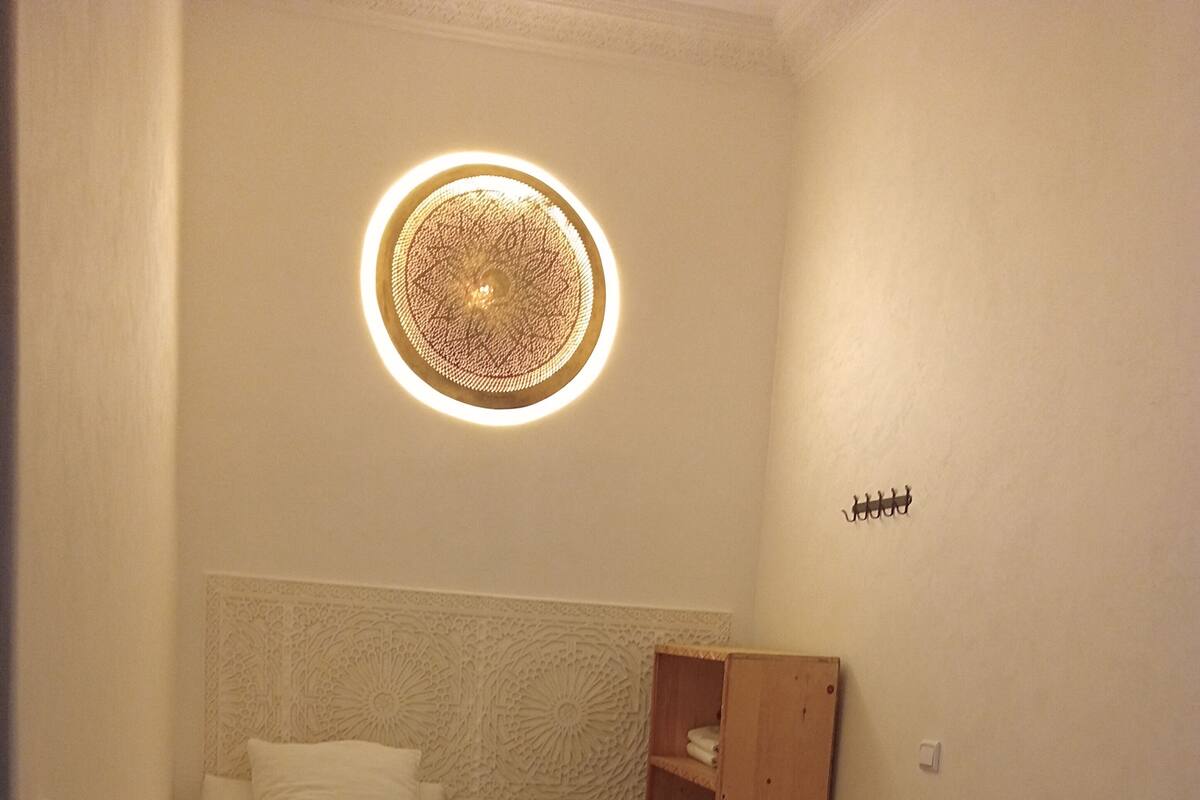 A small, cozy room with two beds, a wooden shelf, and a decorative ceiling light.