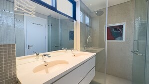 Ein modernes Badezimmer mit großem Spiegel, zwei Waschbecken, einer Dusche und einem Duschbereich mit Glastrennwand.