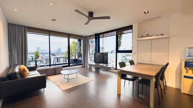 Ein modernes Wohnzimmer mit einer Couch, einem Esstisch und einem Fernseher. Große Fenster bieten Blick auf die Stadt.