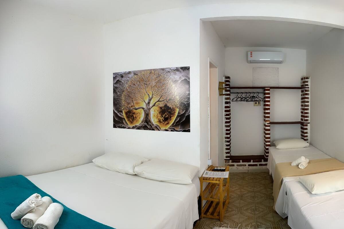 A compact hotel room with two single beds, a small table, a painting on the wall, and a brick-patterned headboard.