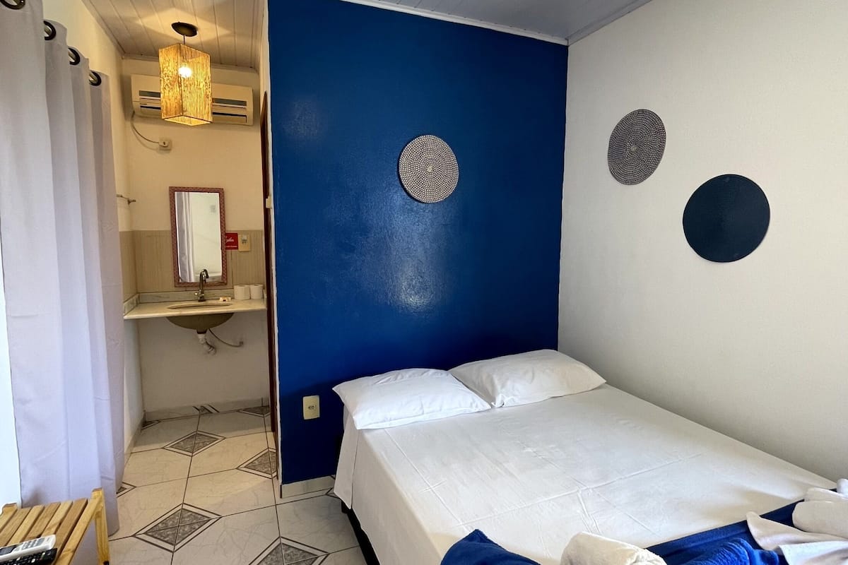 A hotel room with a bed, a small table, a mirror, and a bathroom with a sink and toilet.