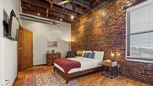 Un dormitorio con cama de madera, pared de ladrillo, ventilador de techo y ventana con persianas.