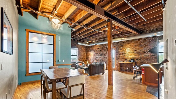 A spacious room with a wooden dining table, a sofa, and a brick wall. - Enjoy downtown living with the comforts of home! (Springfield)