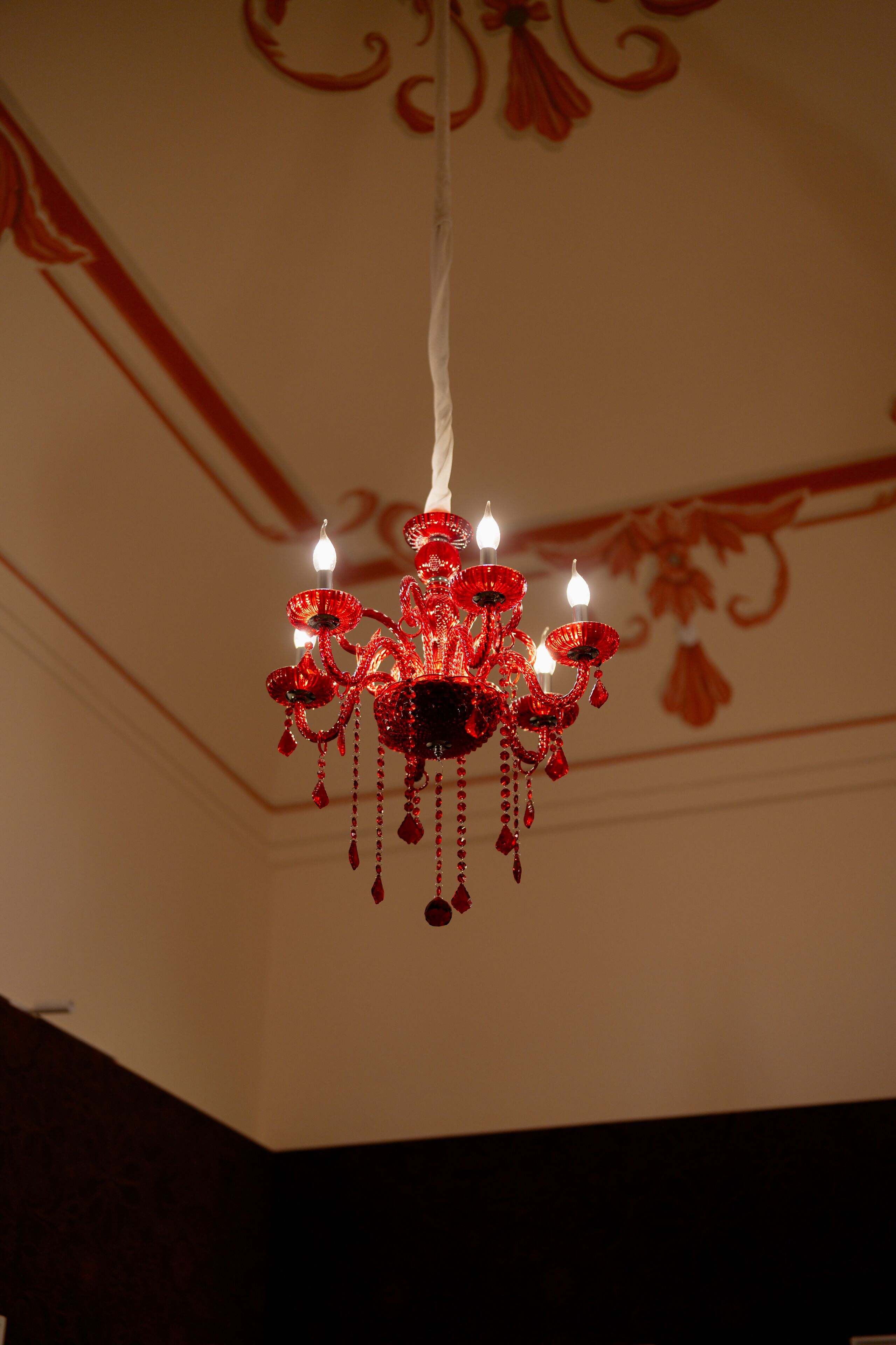 A chandelier with multiple light bulbs hanging from a white ceiling with red floral patterns.