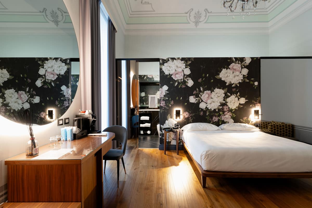 A hotel room with a wooden desk, a bed, a chair, and a mirror.