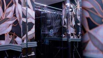 A modern bathroom with a glass shower enclosure, marble walls, and a decorative leaf pattern.