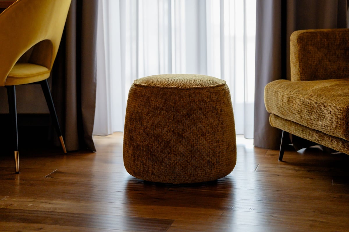 A modern living room with a wooden floor, a round ottoman, a yellow chair, and a brown armchair.