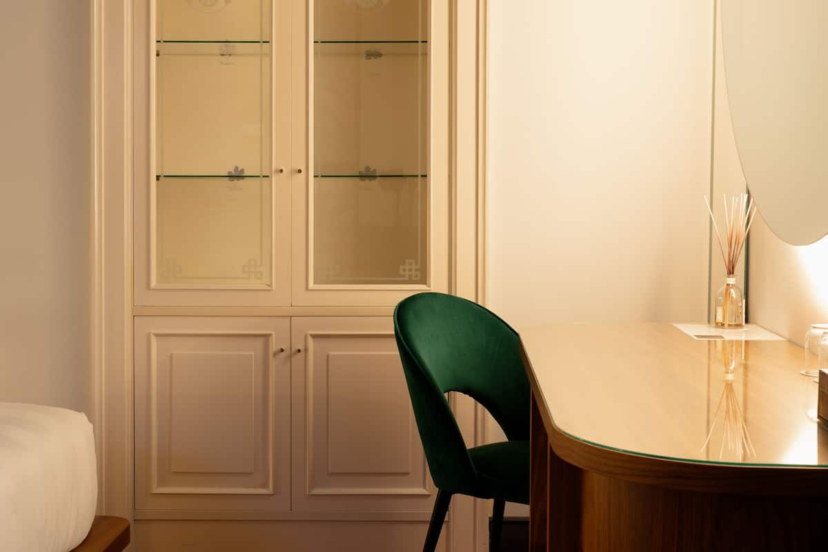 A room with a wooden floor, a green chair, a white bed, and a white cabinet with glass doors.