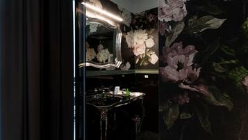 A bathroom with a large mirror, a vanity with a sink, and floral wallpaper.