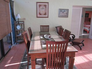 Uma sala de jantar com mesa de vidro, cadeiras de madeira, abajur e quadros nas paredes.