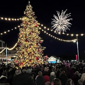 Uma grande árvore de Natal enfeitada com luzes e adornos, rodeada por uma multidão de pessoas.