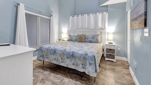 Ein Schlafzimmer mit Bett, Nachttischen, Fenster mit Jalousien und einem Wandbild.