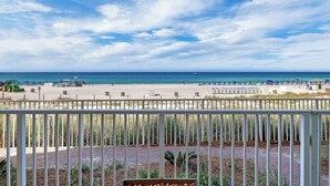 Blick auf den Strand vom Balkon mit weißer Brüstung, Sandstrand und dem Meer im Hintergrund.