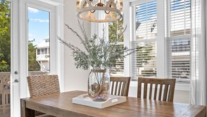 Un coin repas avec une table en bois, deux chaises, un vase avec des branches et un luminaire suspendu.