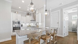Una cocina moderna con armarios blancos, encimera de granito y sillas de madera.