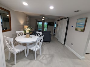 A dining area with a round table and white chairs, a gray sofa, a ceiling fan, and a view of the outdoors. - NEW condo! Just 15 min to Ft Myers and Sanibel beach! Great Location!! (Fort Myers)