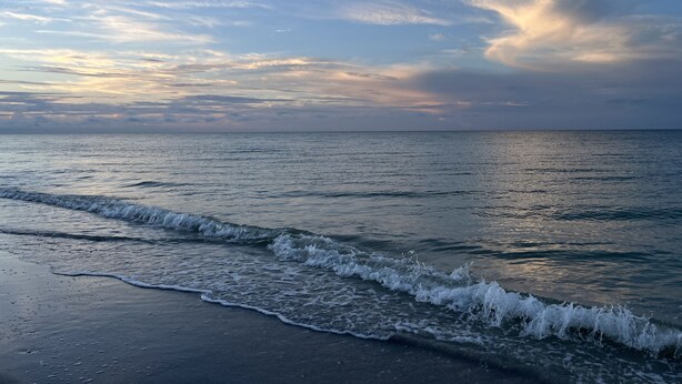 A beach with waves gently lapping onto the shore, under a partly cloudy sky. - NEW condo! Just 15 min to Ft Myers and Sanibel beach! Great Location!! (Fort Myers)