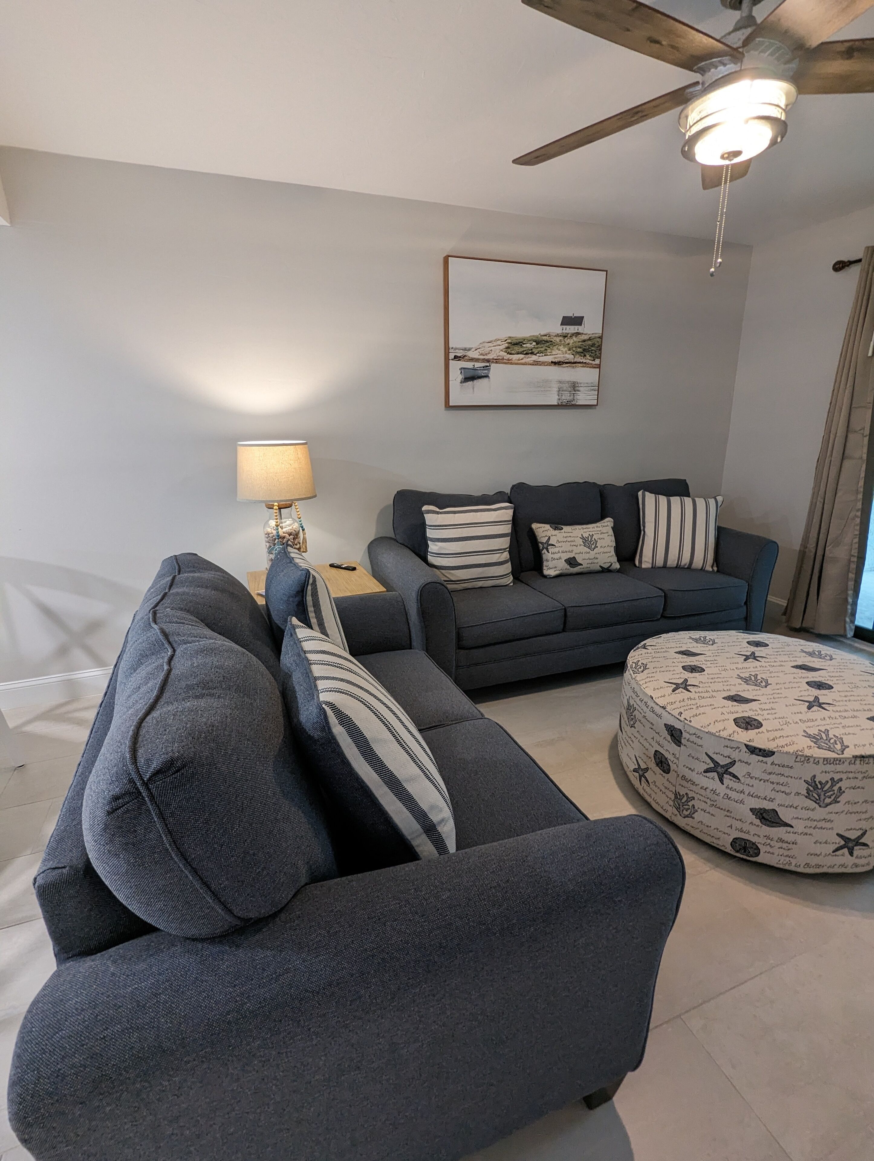 En moderne stue med en grå sofasæt, en rund skammel, en ventilator i loftet og en lampe.