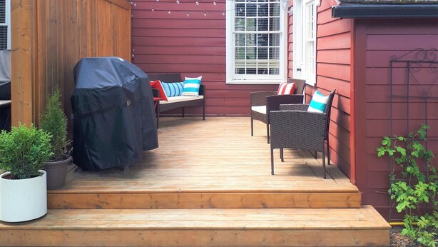 A red house with a wooden deck, two windows, and a covered patio area with outdoor furniture.