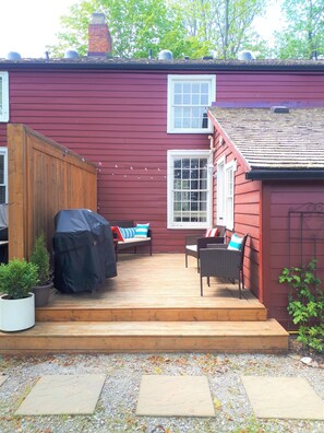 Una casa roja con terraza de madera, dos ventanas y un porche cubierto con mobiliario exterior.