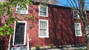 A red two-story house with white shutters, a black front door, and a small porch.