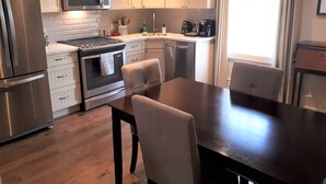 A modern kitchen with stainless steel appliances, white cabinetry, and a dining area with a wooden table and chairs.
