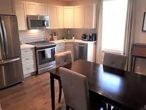 Una cocina moderna con electrodomésticos de acero inoxidable, armarios blancos y un comedor con mesa y sillas de madera.