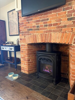 Una habitación con chimenea de ladrillo, un televisor montado encima y una mesa con recipientes metálicos.