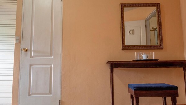 A room with a white door, a mirror on the wall, a small table with a tray, and a bench. - Hotel Arrecifes (San José)